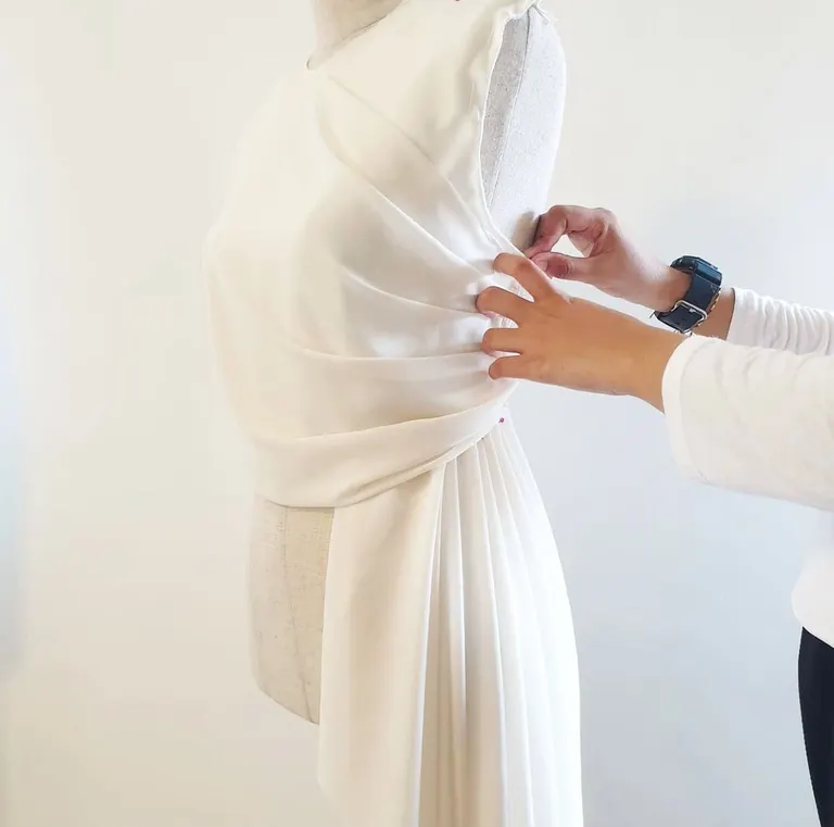 Hands pinning chiffon drapery on a dress form